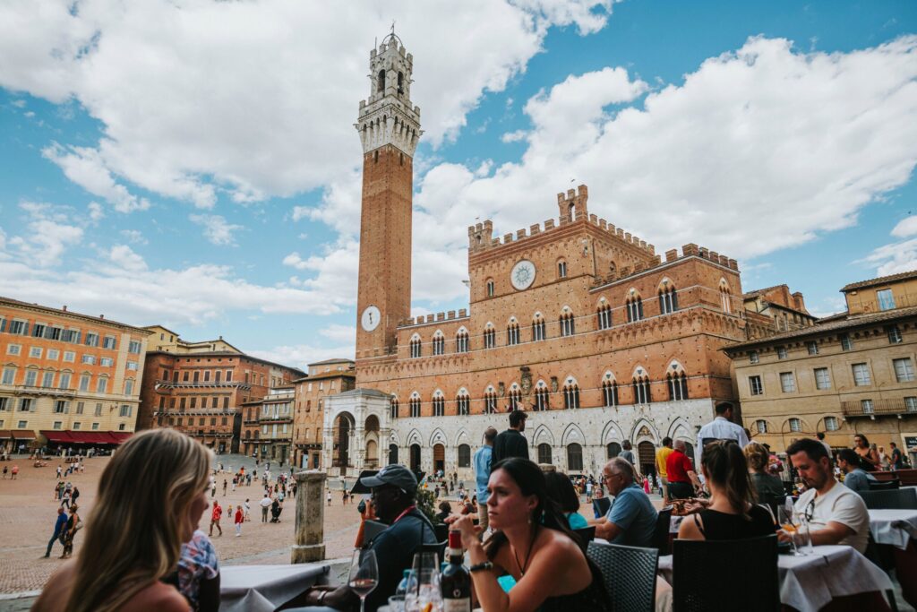 Lively scene at Piazza del Campo, Siena with Torre del Mangia and people enjoying dining outdoors.